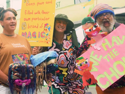 Three people standing in the missle of Newtown Festival, holding bright colourful protest signs.