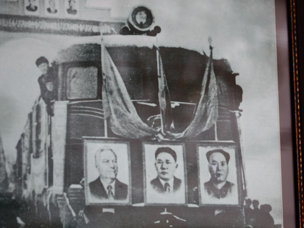 Foto en blanco y negro de un carro o escenario con tres retratos colgados y una figura al lado, ambiente solemne.