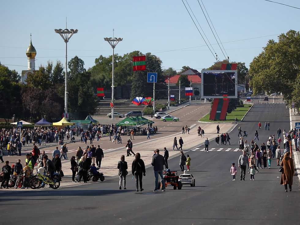 Multitud pasea por una avenida amplia con banderas, quioscos y una iglesia de cúpula dorada al fondo bajo cielo despejado.