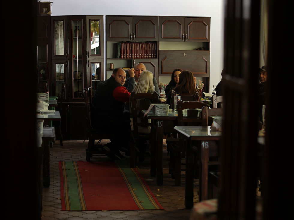 Grupo de personas sentadas en un restaurante oscuro de madera, conversando alrededor de una mesa; alfombra roja y verde.