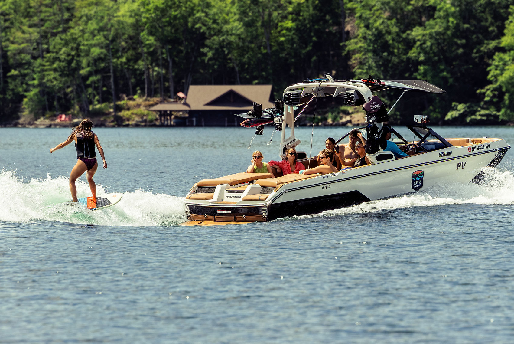 A wake boarder rides the wave behind a wake boat with cheering family.
