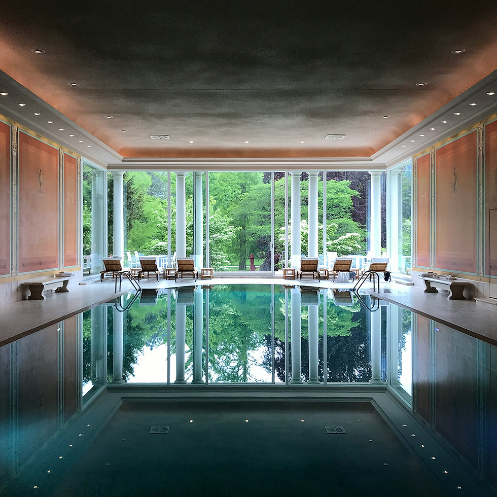 Luxurious indoor swimming pool with large windows overlooking lush green trees.