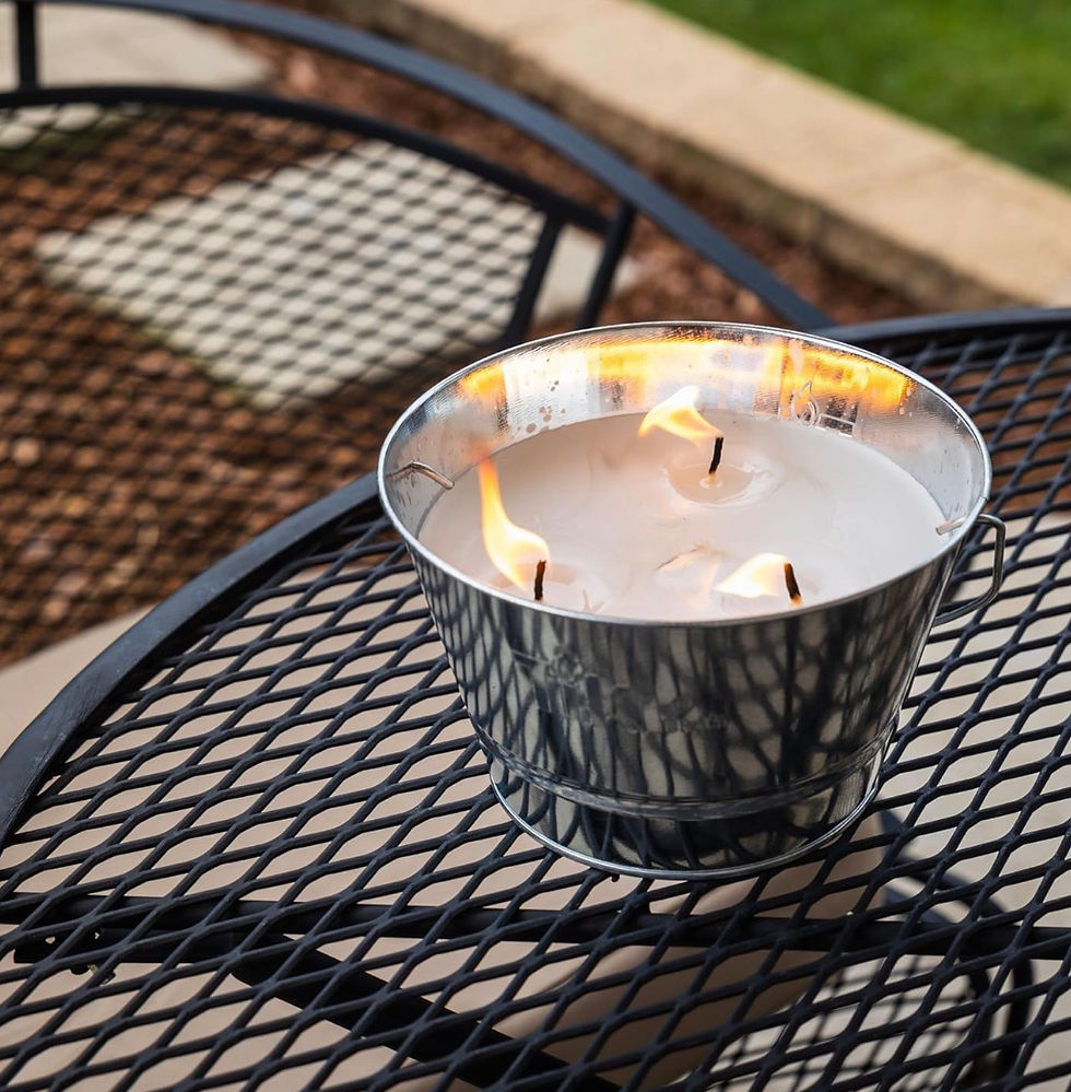 Lit three-wick candle in a silver metal bucket on a black mesh patio table outdoors, with a calm warm glow