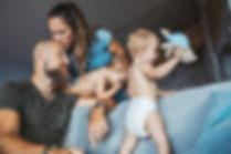 Couple holding their young children and the wife is kissing the dad's head.