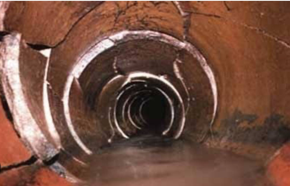 Inside view of a cracked, dark pipe tunnel with water at the bottom. Brown walls with white fractures create an eerie, abandoned atmosphere.