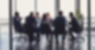Eight adults sitting at a large desk in a corporate environment looking focused during a meeting