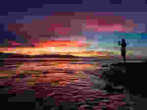 A silhouette of a person taking a picture of a spectacular sunset over Cahuita National Park in Puerto Viejo de Talamanca, Costa Rica.