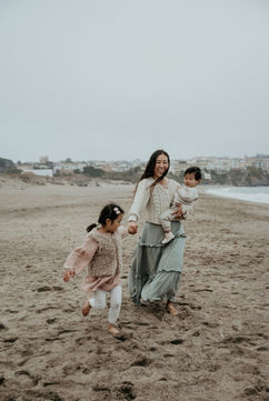 mom is holding toddler boy while daughter is pulling mom on the beach