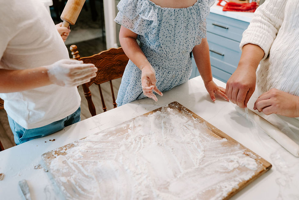 Three people baking, one holding a rolling pin. Flour-covered table, wooden board. Blue kitchen cabinets, cozy atmosphere.