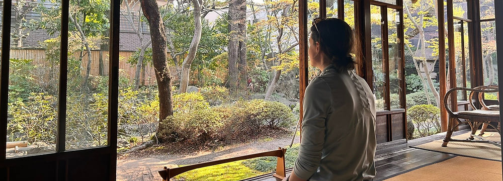 谷中の旧家で畳に正座で座り、日本庭園をゆっくりと眺める女性の後ろ姿。時間が止まったように感じる。
