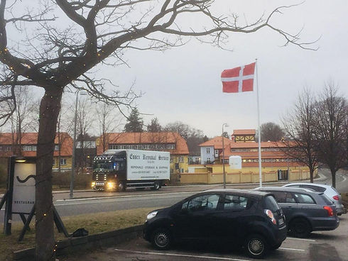 A delivery truck moving along a European street flying a Danish flag