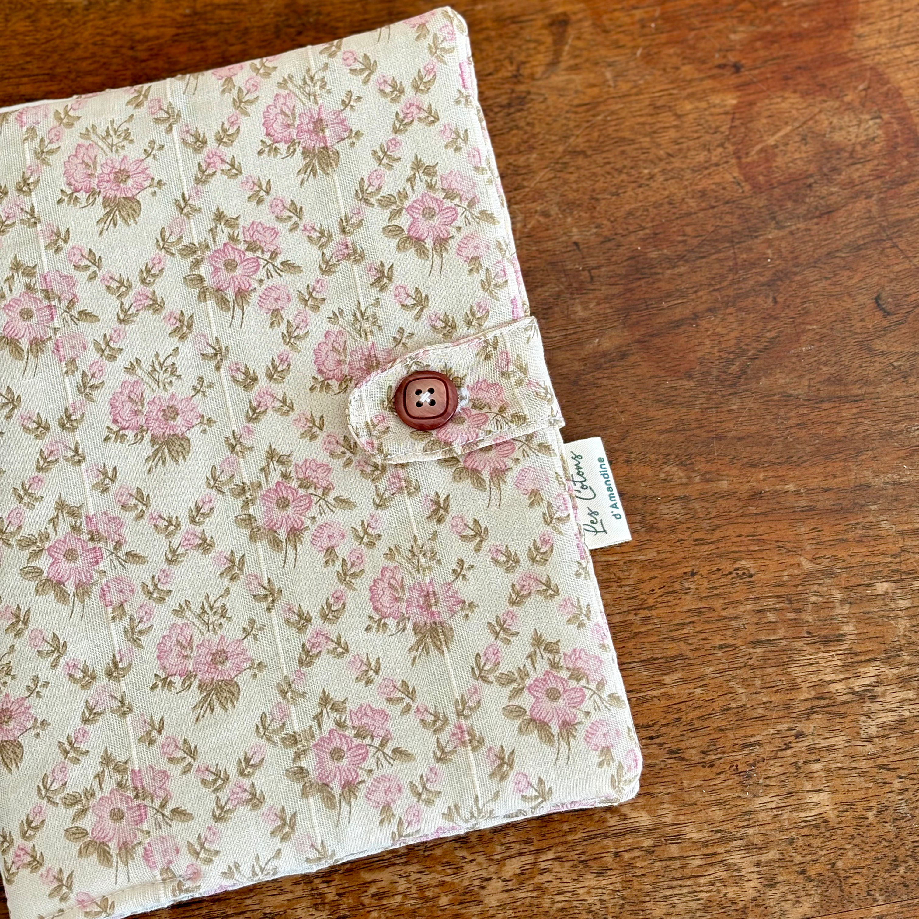protège carnet de santé en tissu écru à fleurs roses, fermé par une patte et un bouton brun rosé
