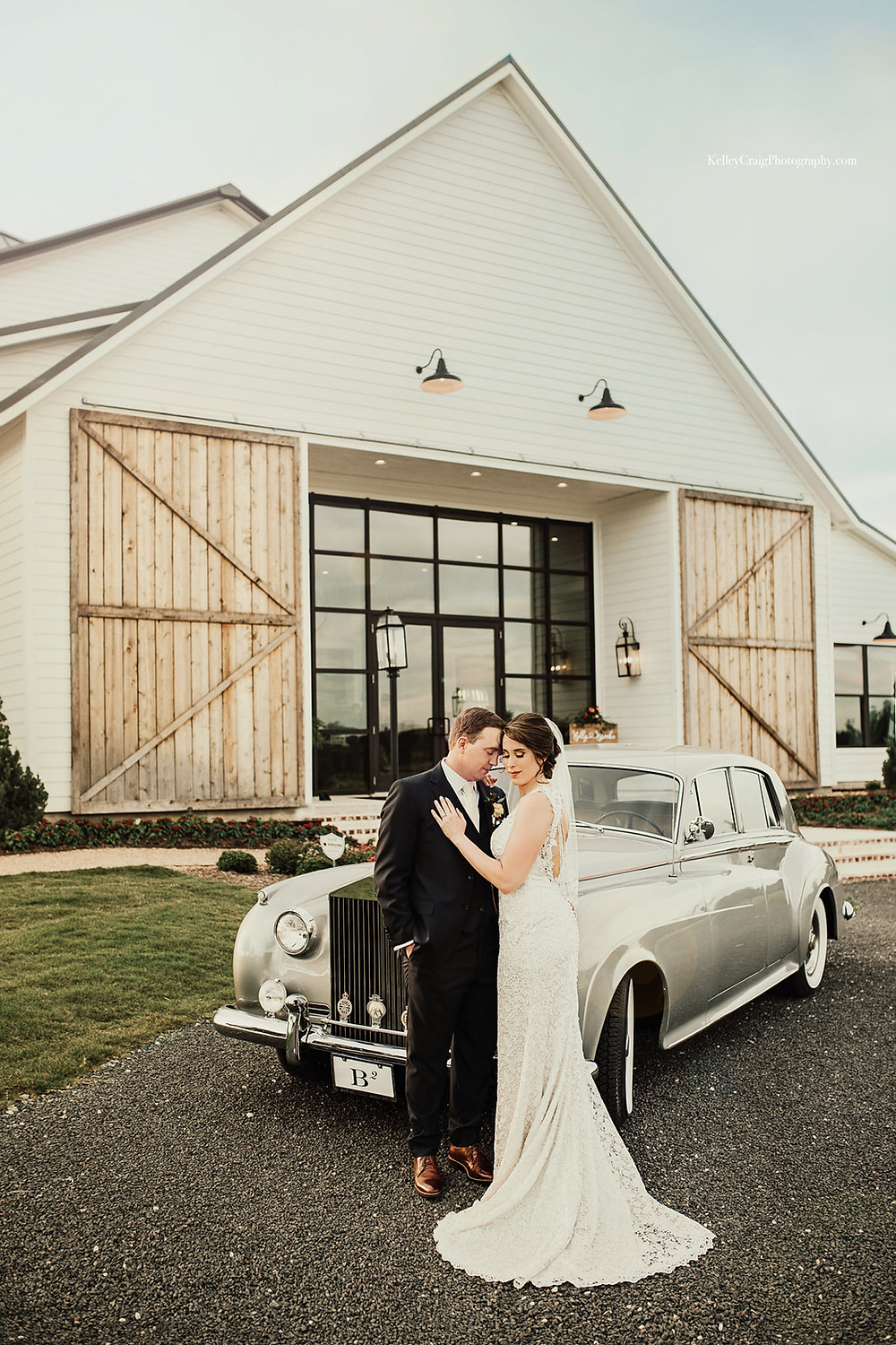 Bride and groom stand in front of Deep in the Heart Farm's reception hall and their classic getaway car.