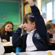 Girl in school uniform raises hand in classroom