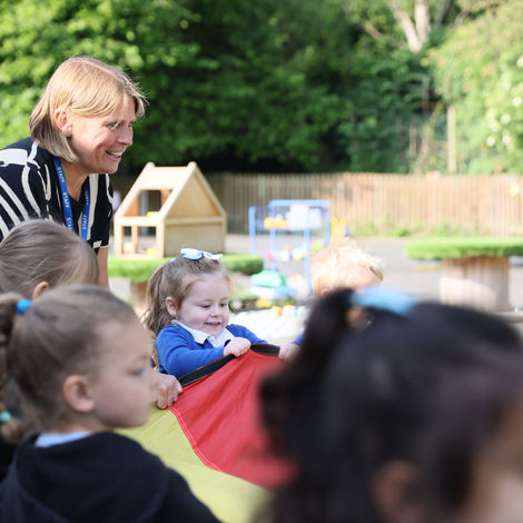 Adult supervising children playing with a colorful parachute