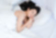 Femme caucasienne avec les cheveux noire qui dort paisiblement. Ses couvertures ainsi que sa camisole de nuit sont blanches.