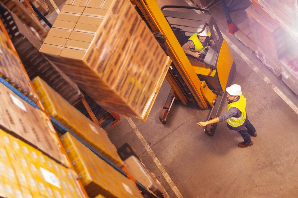 bodega logistica de cadena de suministro, montacargas elevando carga a la estanteria por un montacarguista y un supervisor,