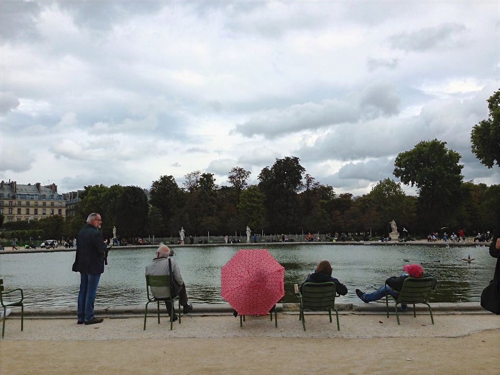 Someone with a red umbrella sitting among other people overlooking a pond in Jardin des Tulleries