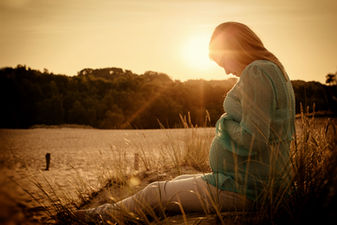Schwangere sitzt in den Boberger Dünen in Hamburg und hält ihren Schwangerschaftsbauch fest
