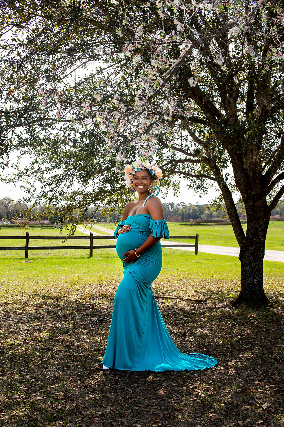 Woman in a stretch teal maternity gown under a tree