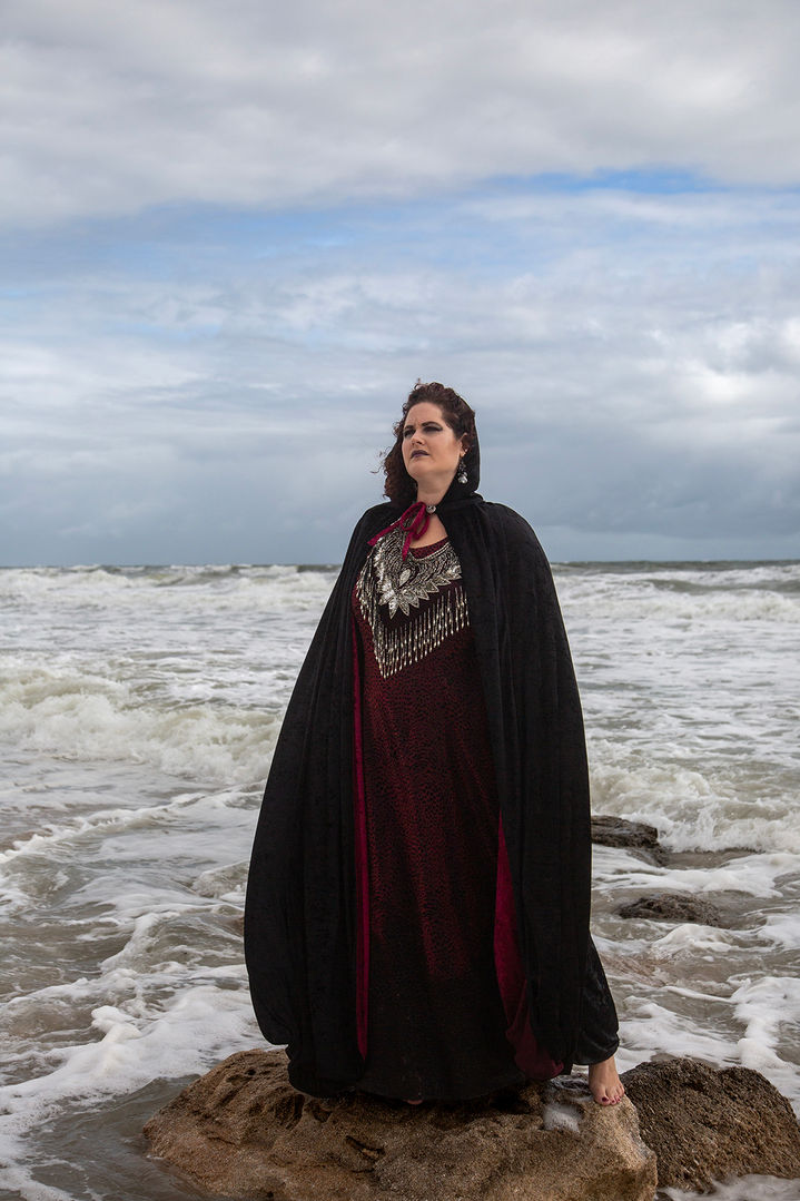 artistic portrait of a woman in a still, dramatic pose, as she stands on a rock in the ocean.