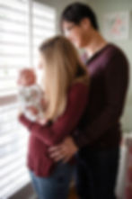Man and woman standing by a window holding their newborn baby