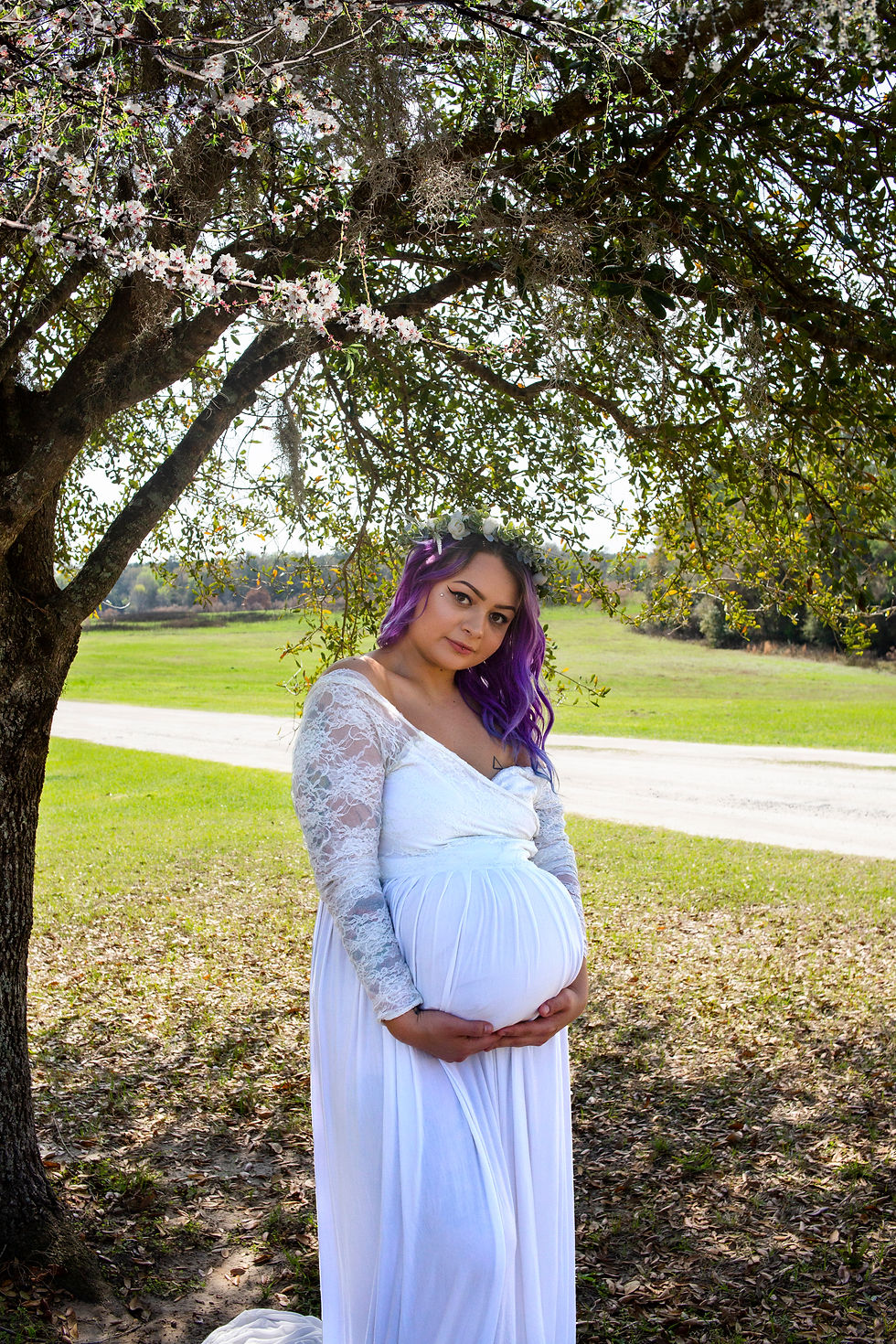 Woman in a white lace maternity gown under a tree