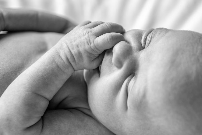 3 week old little girl with hand to face in black and white