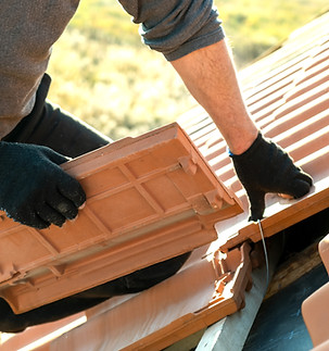 Closeup of worker hands installing yellow ceramic roofing tiles mounted on wooden boards c