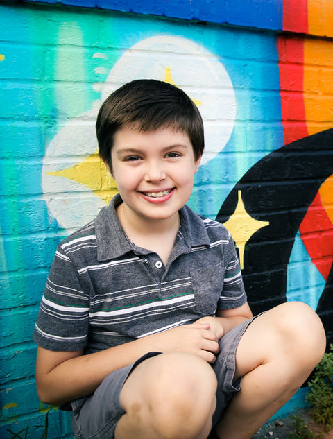 Portrait of a young boy posing in front of a kindness street mural