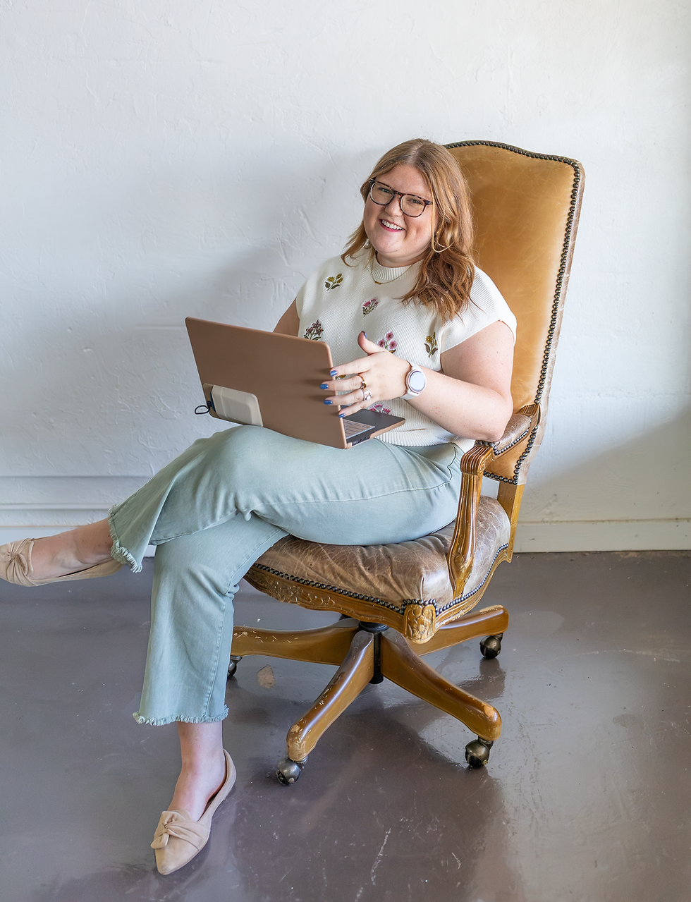 Smiling woman sitting in a yellow chair using a laptop.