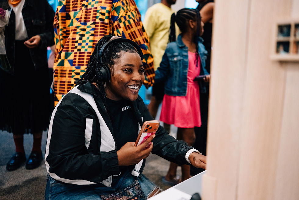 Midtwenties girl with braids wearing headphones smiles while taking in an audio visual work of art at an art exhibition in Detroit, Michigan.
