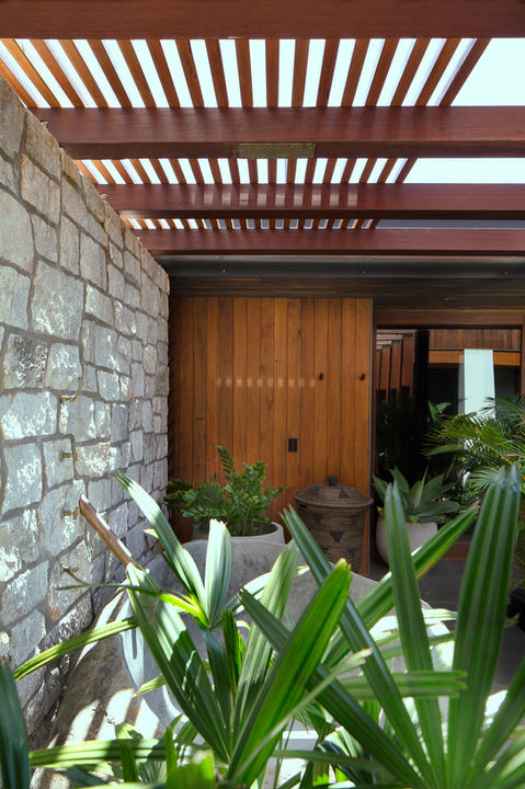 Exterior view of a wooden door and stone wall with plants in front.