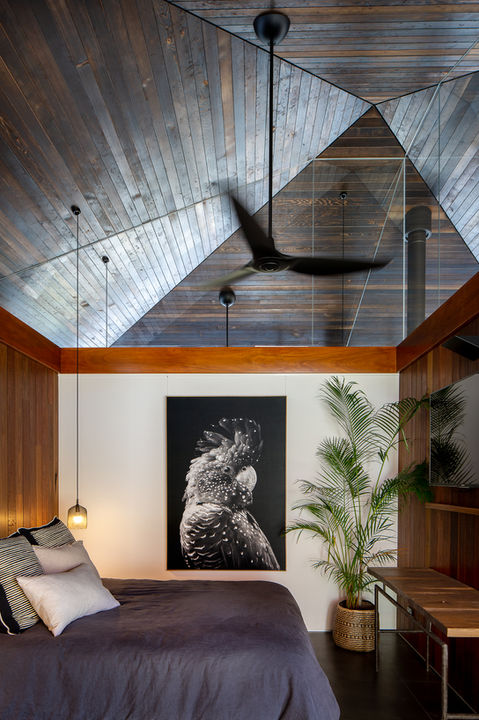 Bedroom with art, plant, wooden ceiling, and hanging fan, creating a relaxing atmosphere.