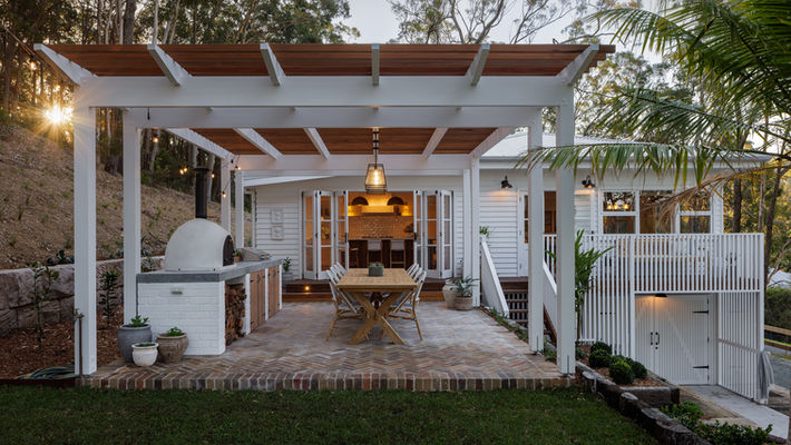 Modern white pergola over a patio with dining table and pizza oven.