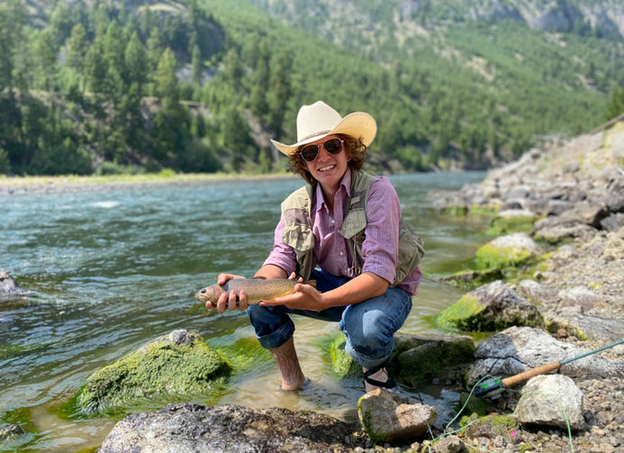 Lukus kneels on the banks of the Yellowstone River holding a beautiful cutthroat trout