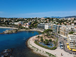 Vue aérienne d’une baie méditerranéenne, promenade bordée de palmiers, immeubles côtiers et mer bleu vif sous ciel clair, Antibes Ponteil.