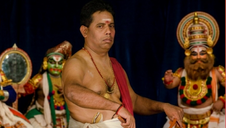 Музыкант играет на chenda drum на фестивале Krishnayanam 2026 в Тривандруме, на фоне артистов Kathakali в традиционных костюмах Кералы.