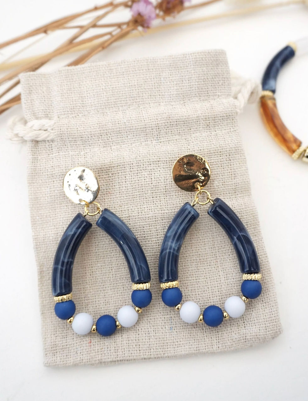 Boucles d'oreilles avec arcs en résine bleue et perles bleues et blanches, accrochées à des attaches dorées texturées.