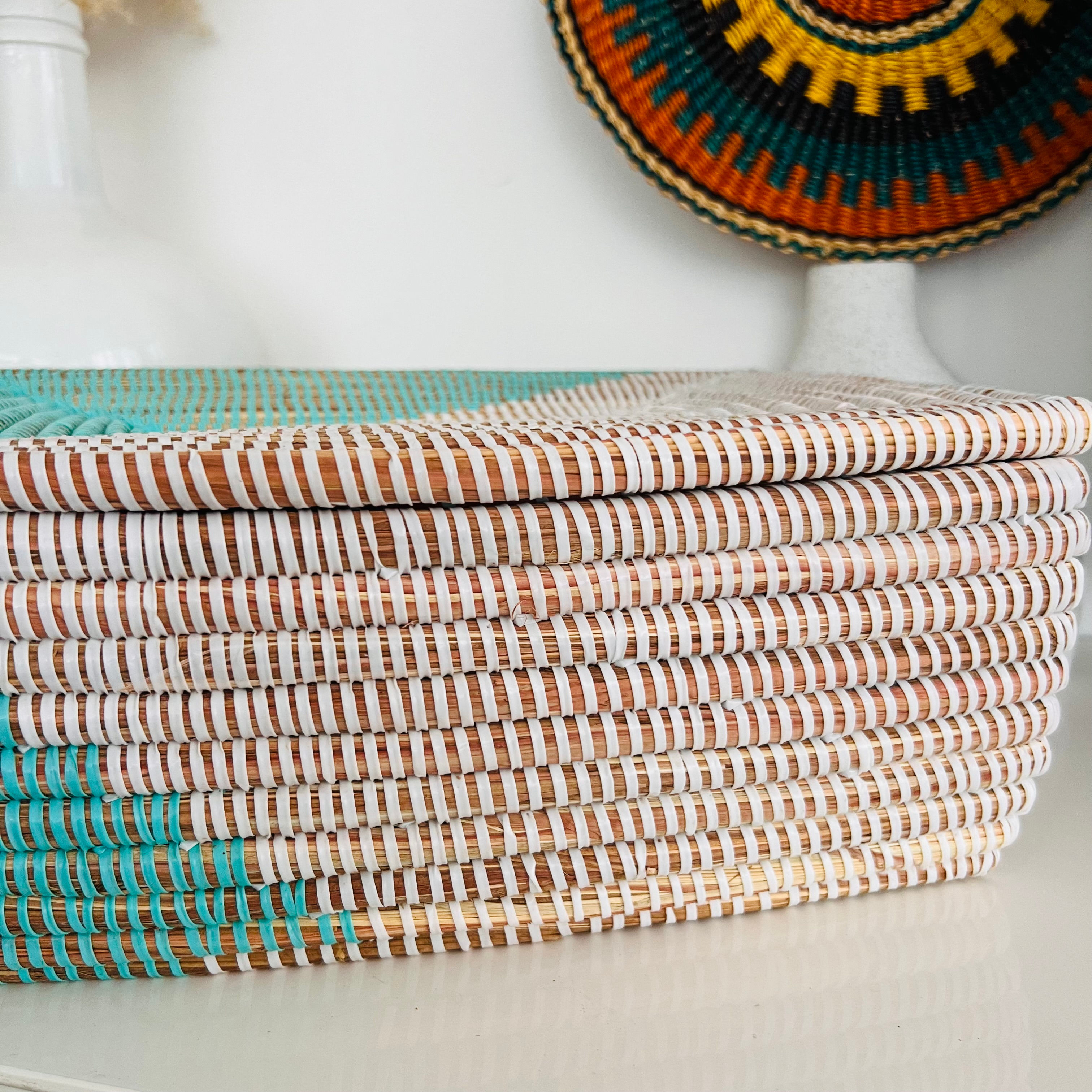 Panier en osier tressé à la main en turquoise et blanc, mesurant 35x12x10 cm, disposé sur une étagère à côté d'un vase en ver