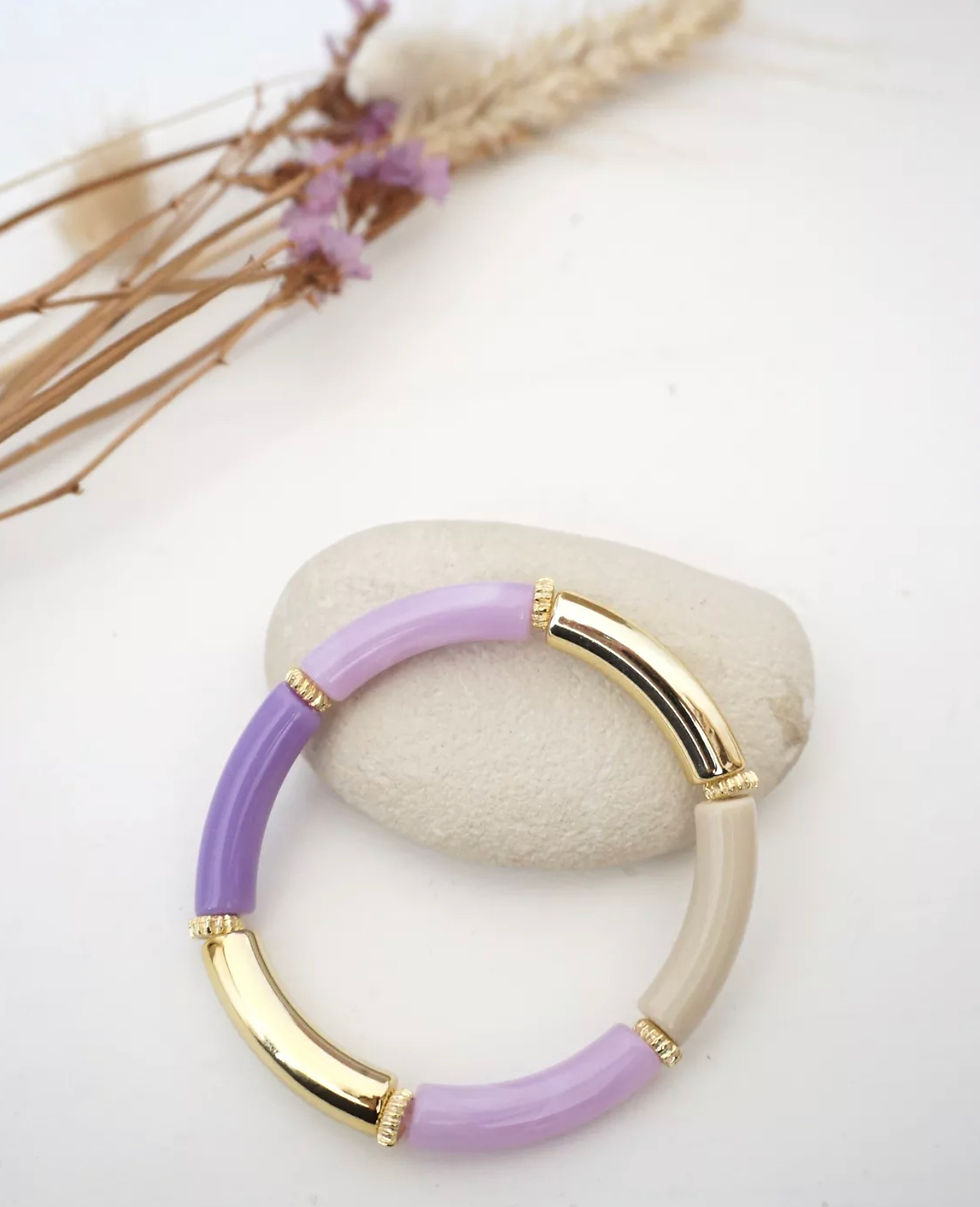 Deux bracelets superposés, l'un en résine lavande et l'autre en ivoire, chacun avec des accents en métal doré, portés au poig