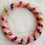 Miniature : Bracelet en perles tissées rose pastel avec des motifs multicolores, posé sur une surface blanche duveteuse.