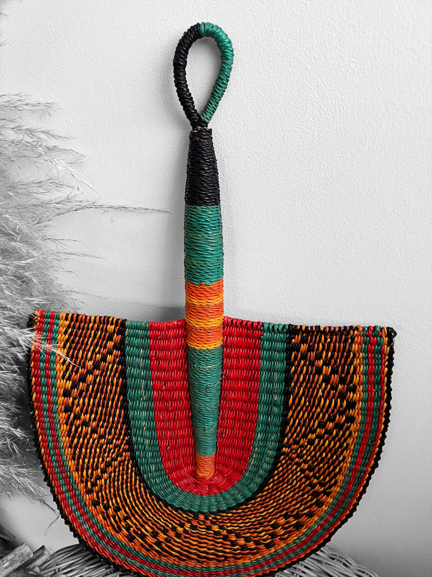 Éventail mural artisanal suspendu, affichant un motif détaillé et coloré, idéal pour rehausser l'esthétique d'un espace de vi