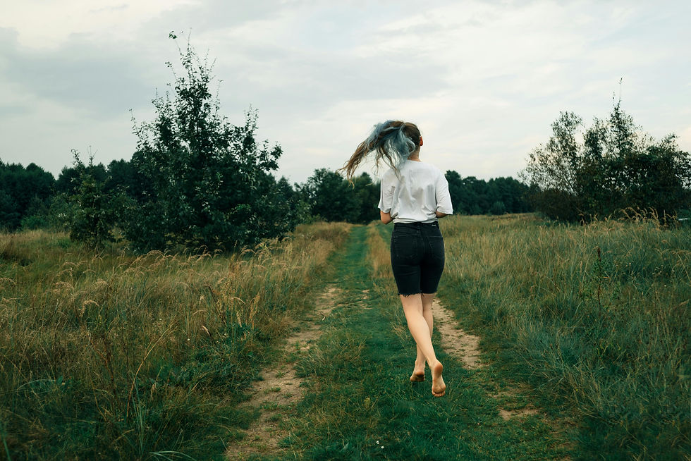 Jeune femme en short noir et t-shirt blanc courant sur un chemin herbeux. Cheveux au vent, ambiance champêtre et ciel nuageux.