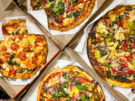 Four colorful pizzas in open boxes, topped with various veggies, meats, and pineapples. Brown boxes with text, vibrant and appetizing scene.