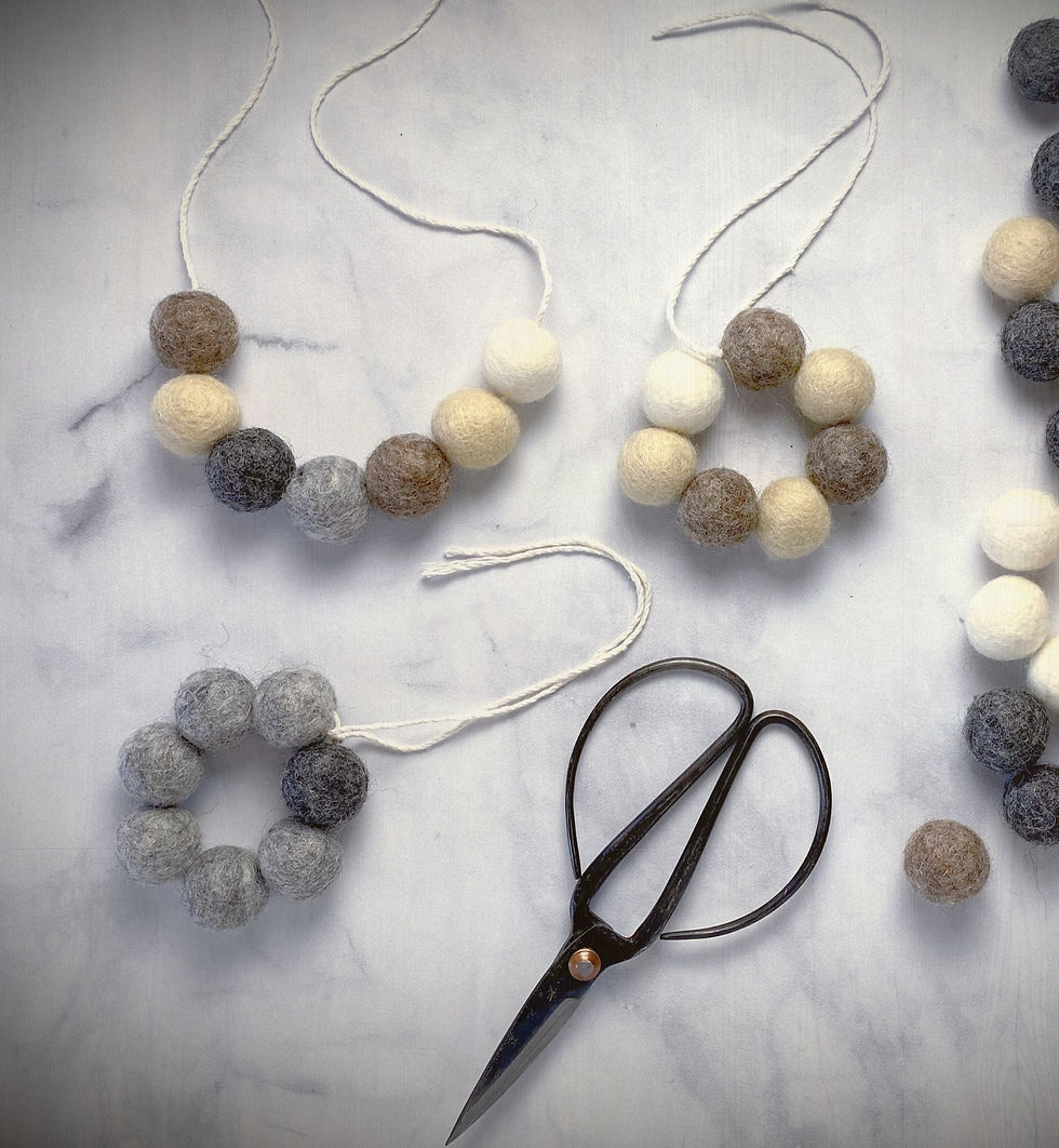 Woolen ball garlands in natural tones on a marble surface. Vintage scissors nearby. Calm, crafting scene.