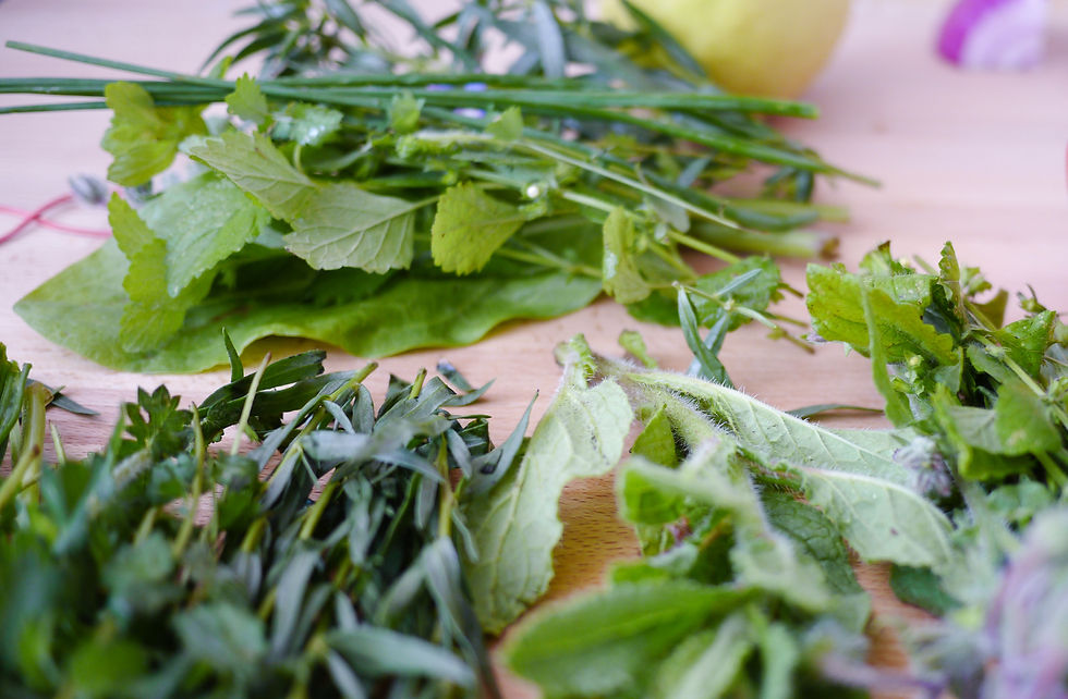 Fresh green herbs scattered on a light wooden surface, with a partially visible lemon and a hint of purple from an onion in the background.