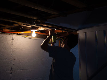 Man working on wiring in the basement with a single light bulb turned on. 