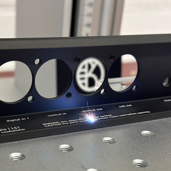 Een zwart geanodiseerd aluminium audiopaneel dat bij KRABER wordt voorzien van een lasergravering. Het door KRABER gegraveerde paneel wordt uiteindelijk in een speaker geplaatst.