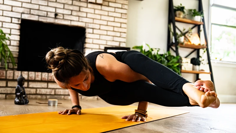 woman doing yoga in 8 legged pose arm balance on an orange yoga mat on a wooden floor